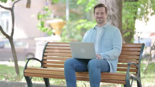 Smiling Man Working on Laptop Sitting on Bench