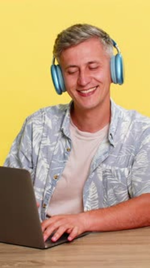 Man in Wireless Headphones Working on Laptop at Table Nodding Head Enjoying Favorite Music Sound