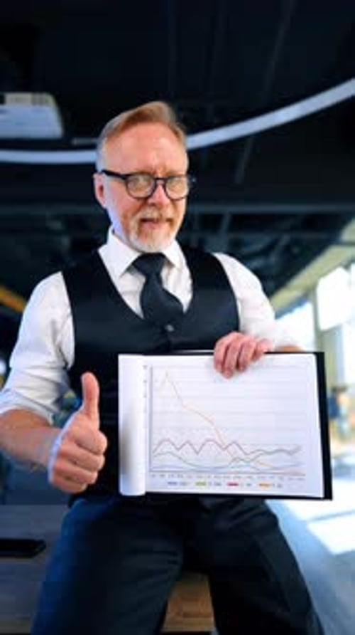 Man in eyeglasses showing the paper with graphs and his thumb up enjoying result.