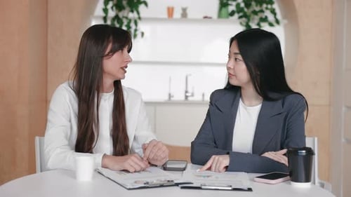 Two Women Discuss Data Report at Table