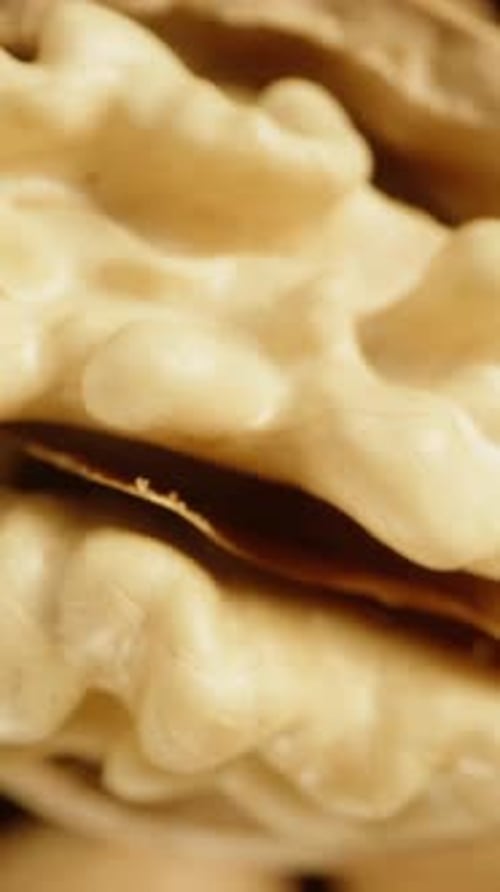 Vertical view of a partially peeled walnut slowly rotating and falling down among a pile of other