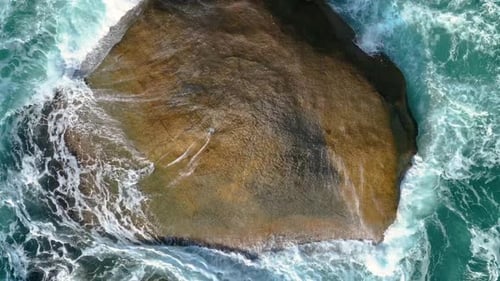 Aerial drone view of foamy waves breaking on a rocky shore.