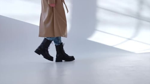 Casual style presentation in the studio. Girl wearing black combat boots, jeans and coats walks