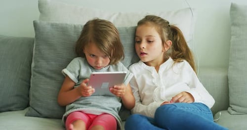 Young Girls Using Tablet Device on Gray Couch
