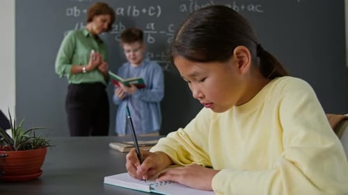 Porträt eines lächelnden asiatischen Mädchens, das im Klassenzimmer in ihr Notizbuch schreibt