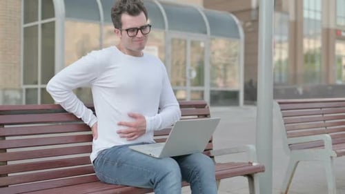 Man Using Laptop Experiences Back Pain on Bench