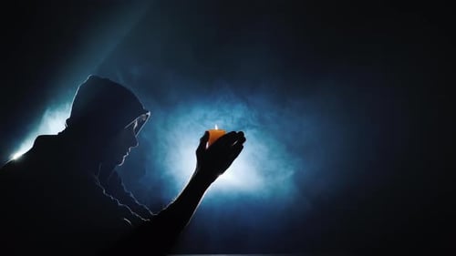 Silhouette Holding Candle Flame in Darkness with Smoke