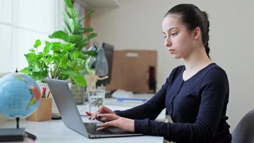 Woman Typing on Laptop, Drinks Water at Desk