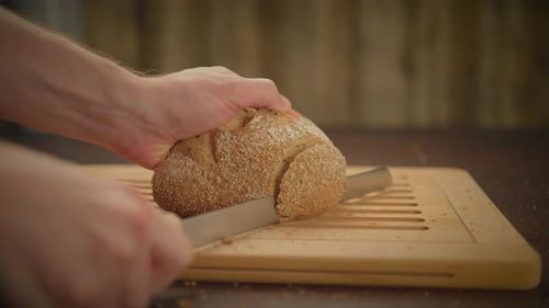 Person Slicing Loaf of Bread on Cutting Board