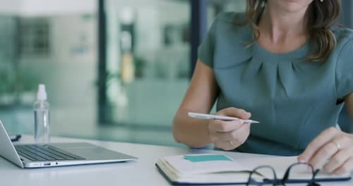 4k video footage of a young businesswoman using a laptop and writing notes in a modern office