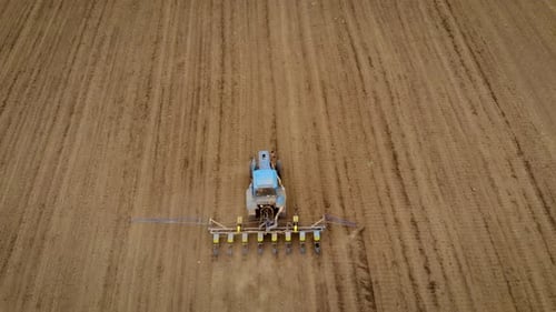 Aerial View of Dusty Tractor Rides on Field and Sows Seeds