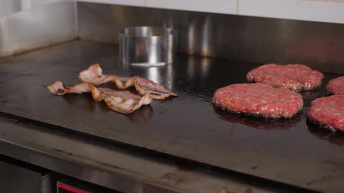 Closeup of Bacon and Burger Patties Fried on a Stove in the Restaurant Kitchen