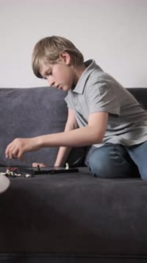 Menino jogando xadrez em casa sentado confortavelmente no sofá cinza dentro de casa