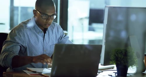 4k video footage of a young businessman working late on a computer and laptop in an office