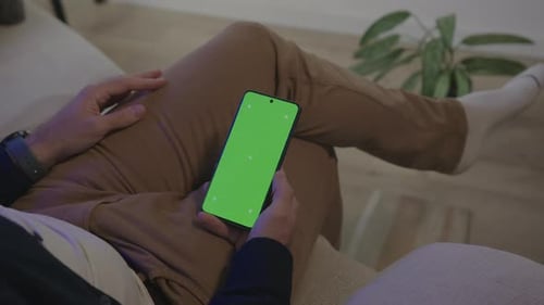 Man Sitting With Legs Crossed On The Sofa, Using Smartphone With Green Screen. high angle shot