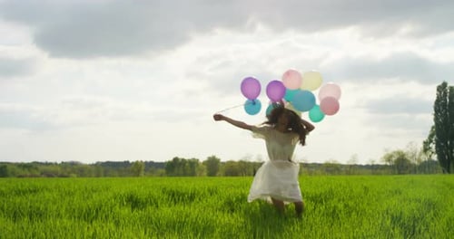 Young Woman Running with Balloons in Green Field