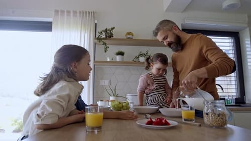 Father pours milk for children in kitchen