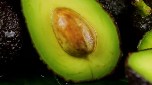 Drops of water fall on avocado fruits with leaves on a black background. Raw Fruits, healthy food.