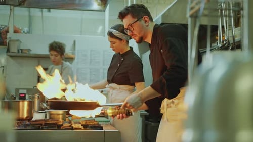 Chef Cooking Dish in Skillet with Blow Torch in Restaurant Kitchen