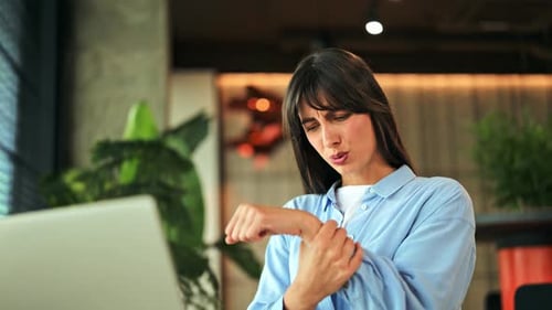 Professional Woman Experiencing Wrist Pain While Working on Laptop in a Modern Office Setting