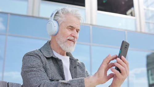 Elderly Male Person with Headset Using Modern Phone in City