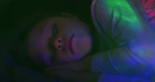 Sleeping Child Illuminated by Colorful Lights at Night