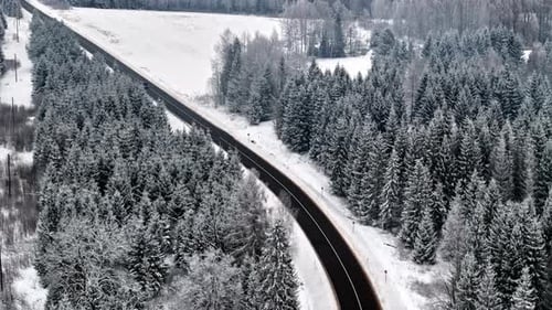 Aerial view of a winding snowy road through a serene winter forest landscape
