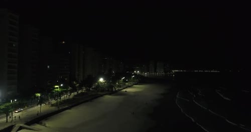 Drone strolling along the beach on top of the sand strip showing city in the background and lights,