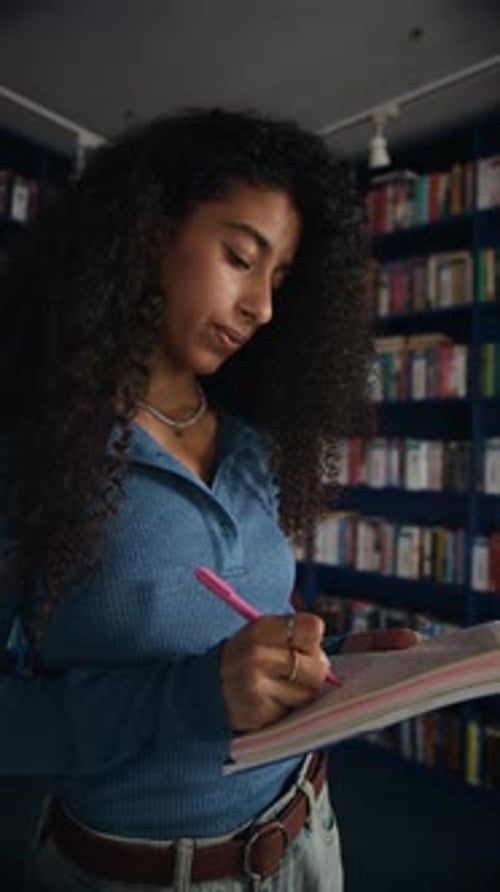 Smart Female Student Taking Notes in Library in front of Bookshelf