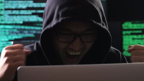 Close de Hacker in a Hood comemorando o sucesso do ataque de servidores de infraestrutura global por meio de um laptop