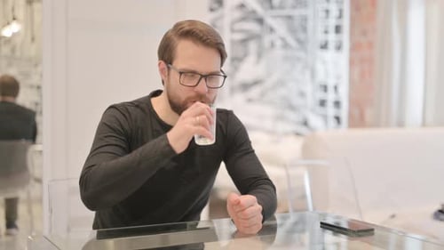 Junger Mann trinkt Wasser, während er zu Hause sitzt