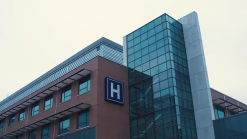 Panning exterior shot of a hospital building with the letter H sign displayed on the side