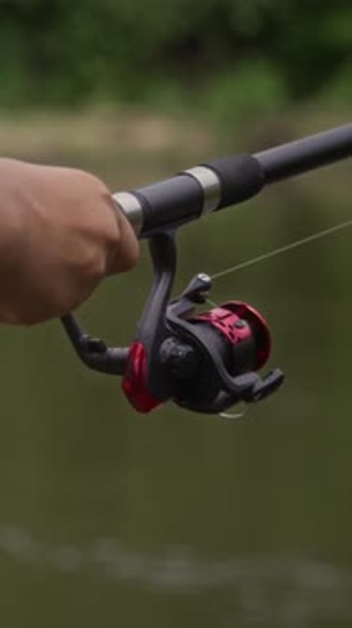 Hände eines unbekannten Anglers, der beim Angeln am Fluss Rolle auf Rute aufwickelt