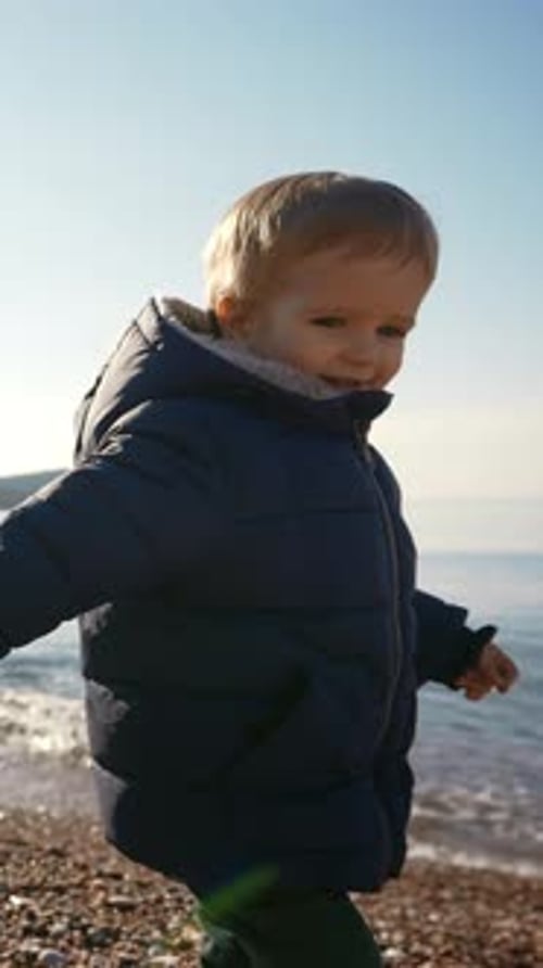 Child Walks Along Pebble Beach in Winter Coat