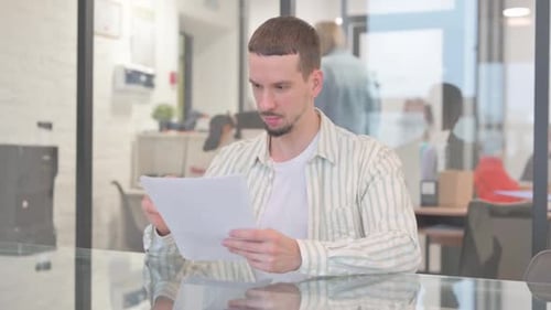 Young Adult Man Reviews Documents at Office Desk