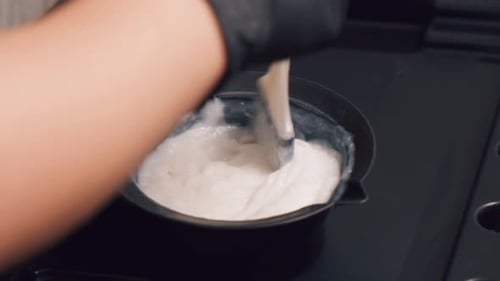 Gloved Hand Mixing White Cream in Black Bowl