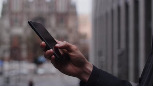 Cropped View of a Businessman Tapping on the Phone Screen on Blurred City Background