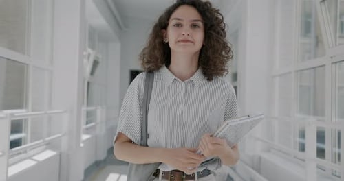 Dolly Shot of Beautiful Young Woman Walking in University Hallway Holding Books Waving Hand Greeting