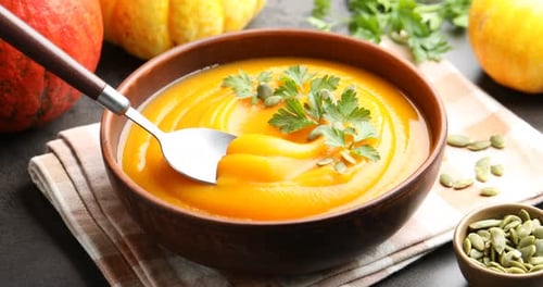 Taking tasty pumpkin cream soup with spoon from bowl on table, closeup