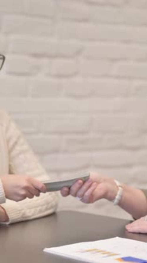 Woman Passes Stack of Money to Man at Table