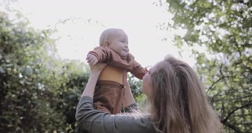 Single mother lifting baby in garden and playing in sunshine
