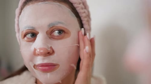 Woman Applying Cosmetic Face Mask in Mirror