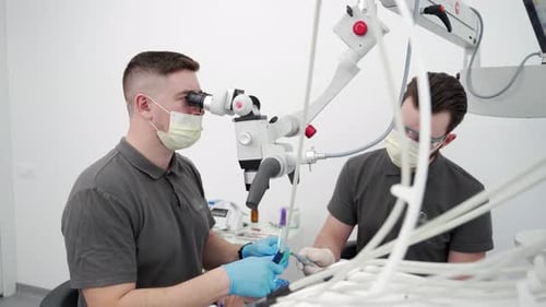 Odontólogo masculino que trata endodoncias con microscopio en una clínica de estomatología moderna, asistente dental