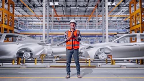 Corps entier d'un ingénieur asiatique souriant et tapant dans ses mains dans une usine automobile