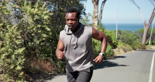 Man Running on Road Next to Ocean and Trees
