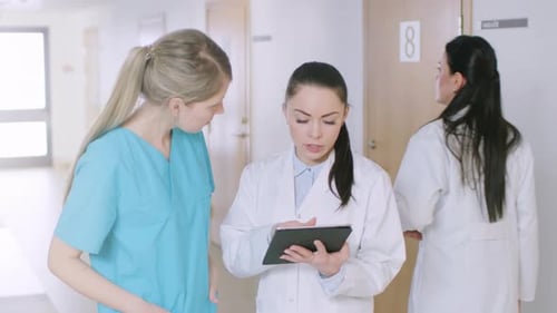 In the Hospital, Busy Doctors Talk, Using Tablet Computer While Standing in the Hallway. New Modern
