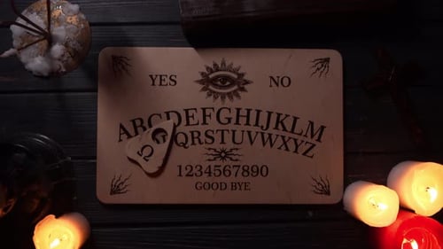 Close Up Video of a Wooden Ouija Board on a Table Surrounded By Candles Candlesticks and Other