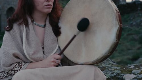 spiritual woman peacefully playing a shamanic drum in a beautiful medieval village close detail shot