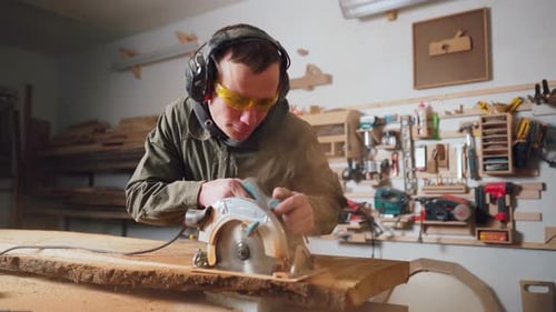 Man Cutting Lumber in Workshop With Power Saw