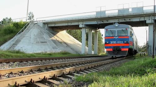 Elektrischer Personenzug bewegt sich schnell unter einer Autobrücke auf der Eisenbahn